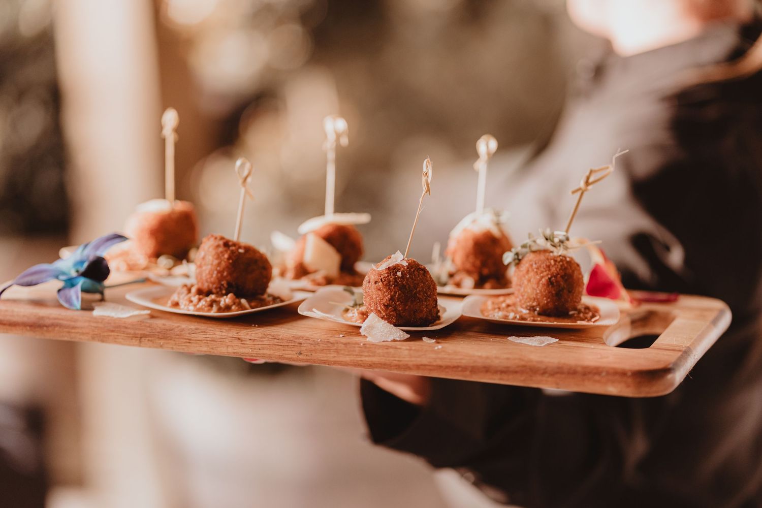 Elegant wooden tray of breaded appetizer bites with decorative picks served at wedding reception.