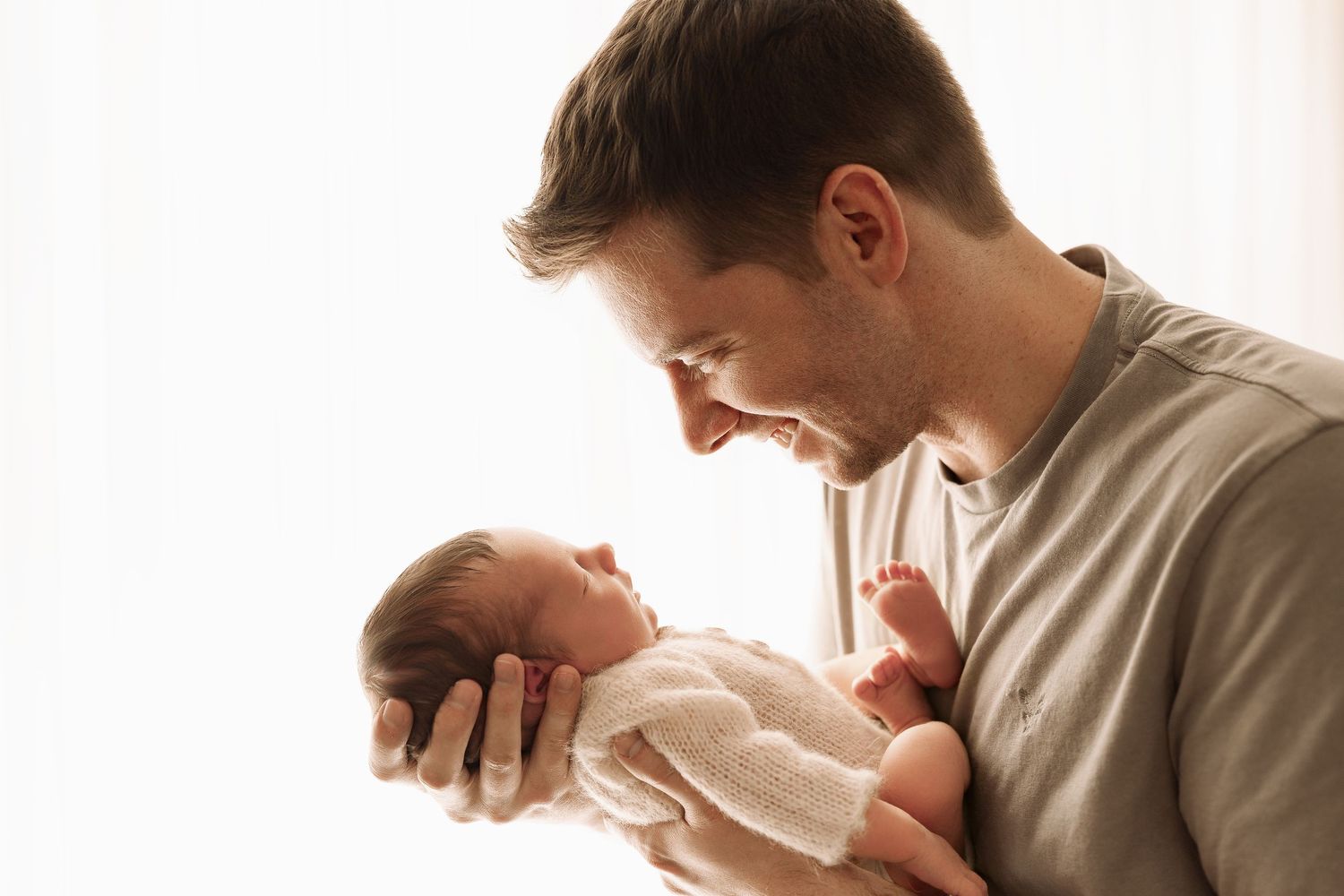New father tenderly gazing down at his sleeping newborn baby held gently in both hands.