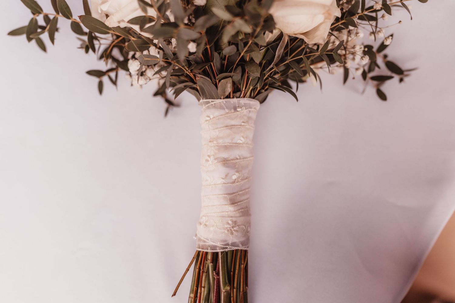 Close-up of a white rose and eucalyptus bridal bouquet with lace-wrapped stems.