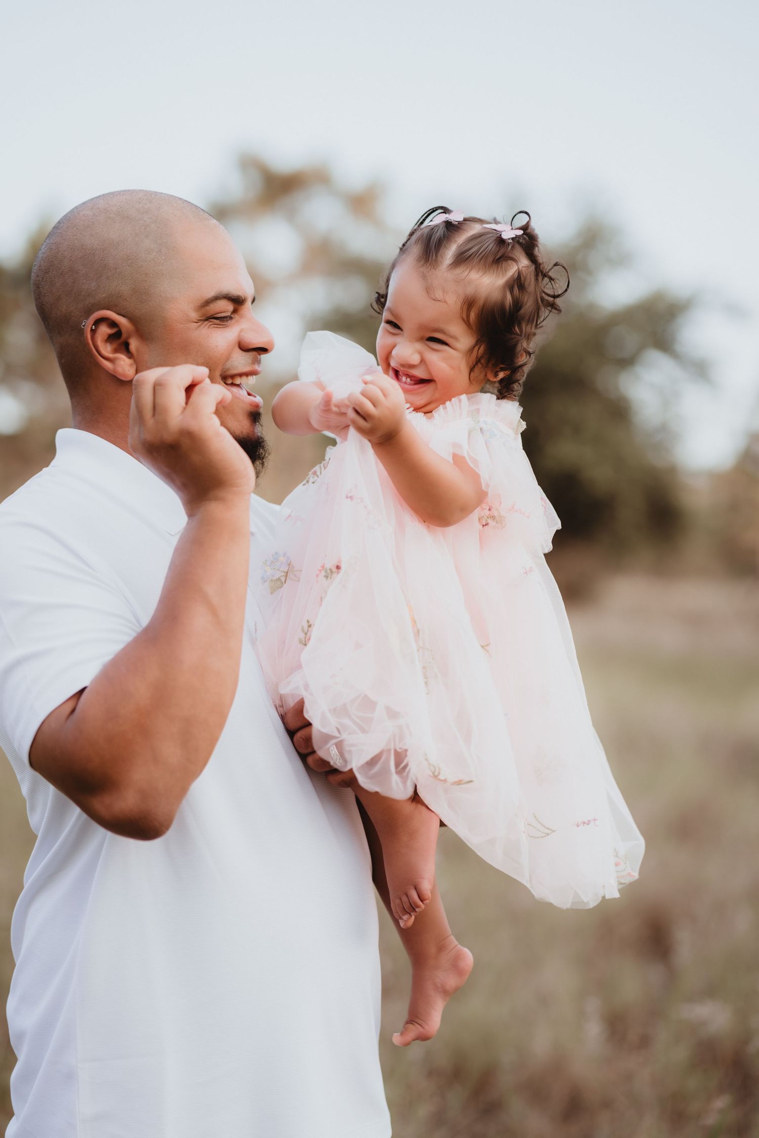 Loving father in white shirt holding his laughing toddler daughter in a pink tutu dress.