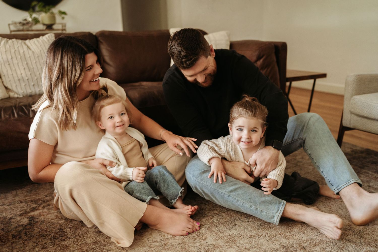 Happy family of four sitting together on a carpet, smiling and bonding in a warm living room.