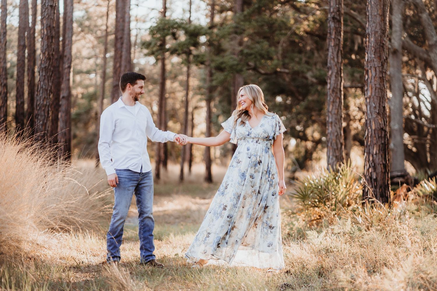 Joyful expecting couple holding hands and laughing in a sunlit pine forest.
