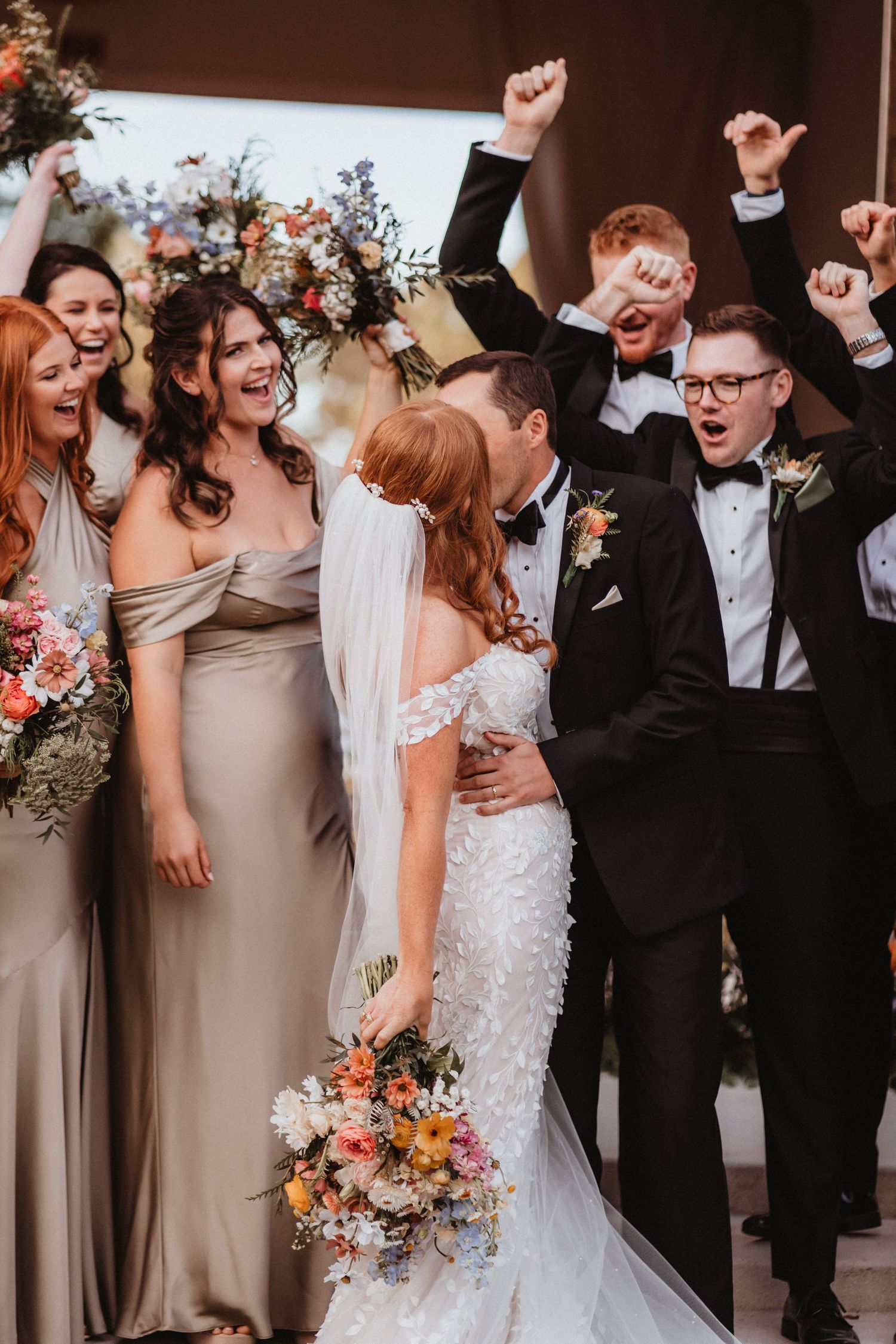 Excited wedding party cheers as bride and groom share a romantic kiss at the altar.