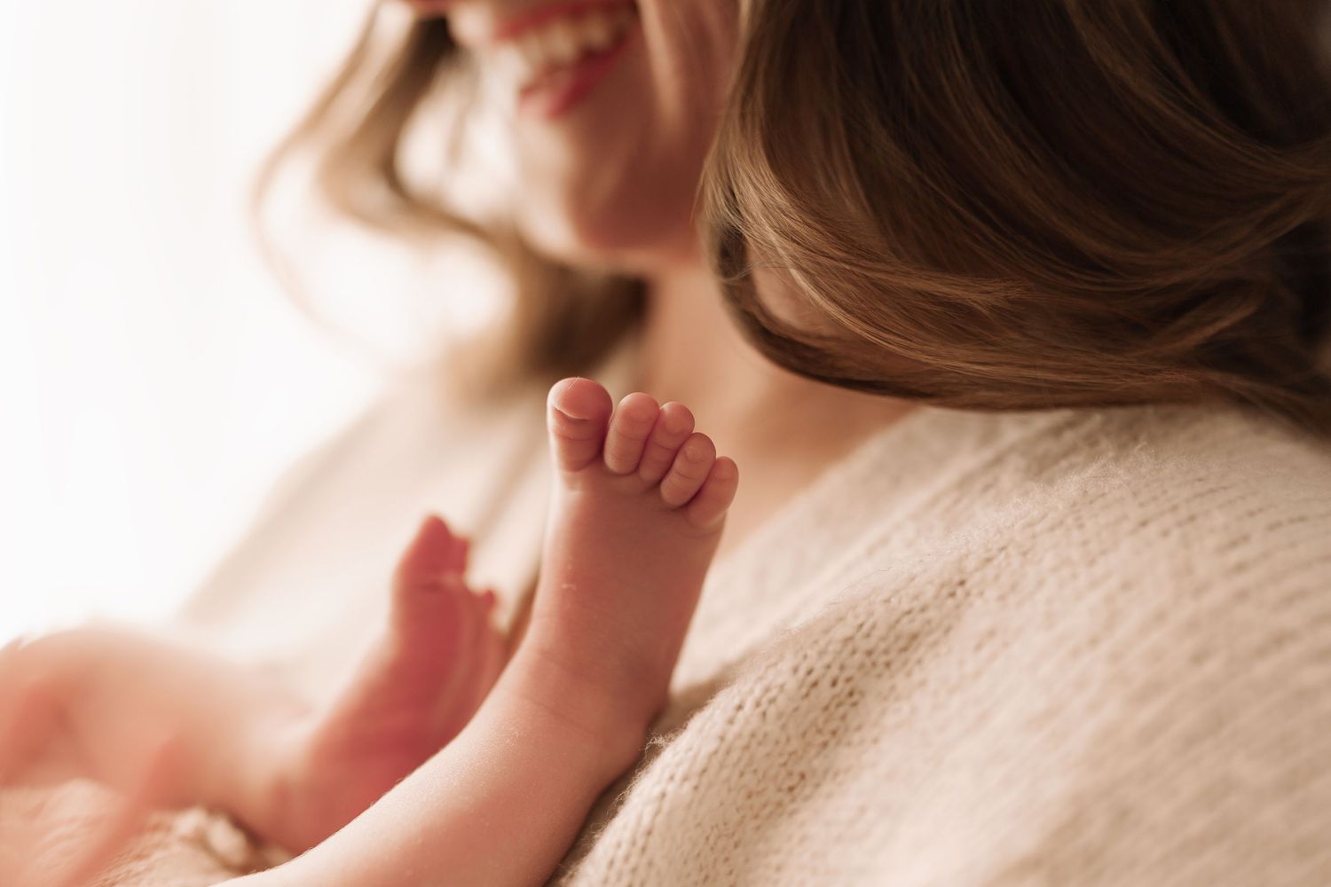 Close-up of a newborn babys tiny hand resting against a mothers cream knit sweater.