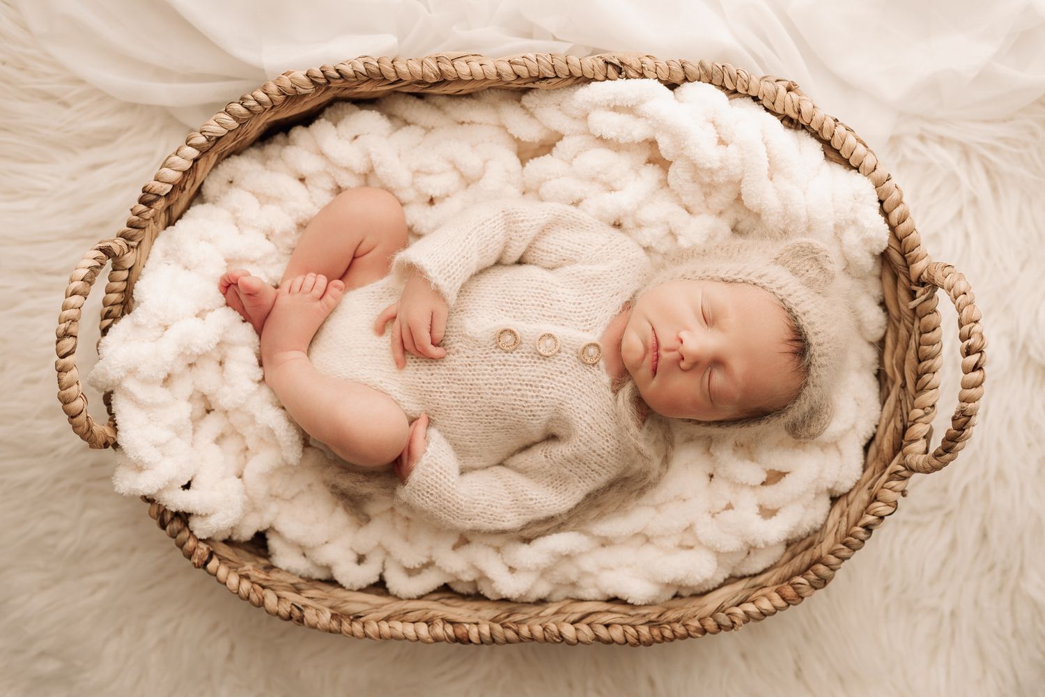 Peaceful newborn baby sleeping in a wicker basket lined with white fluffy blanket.