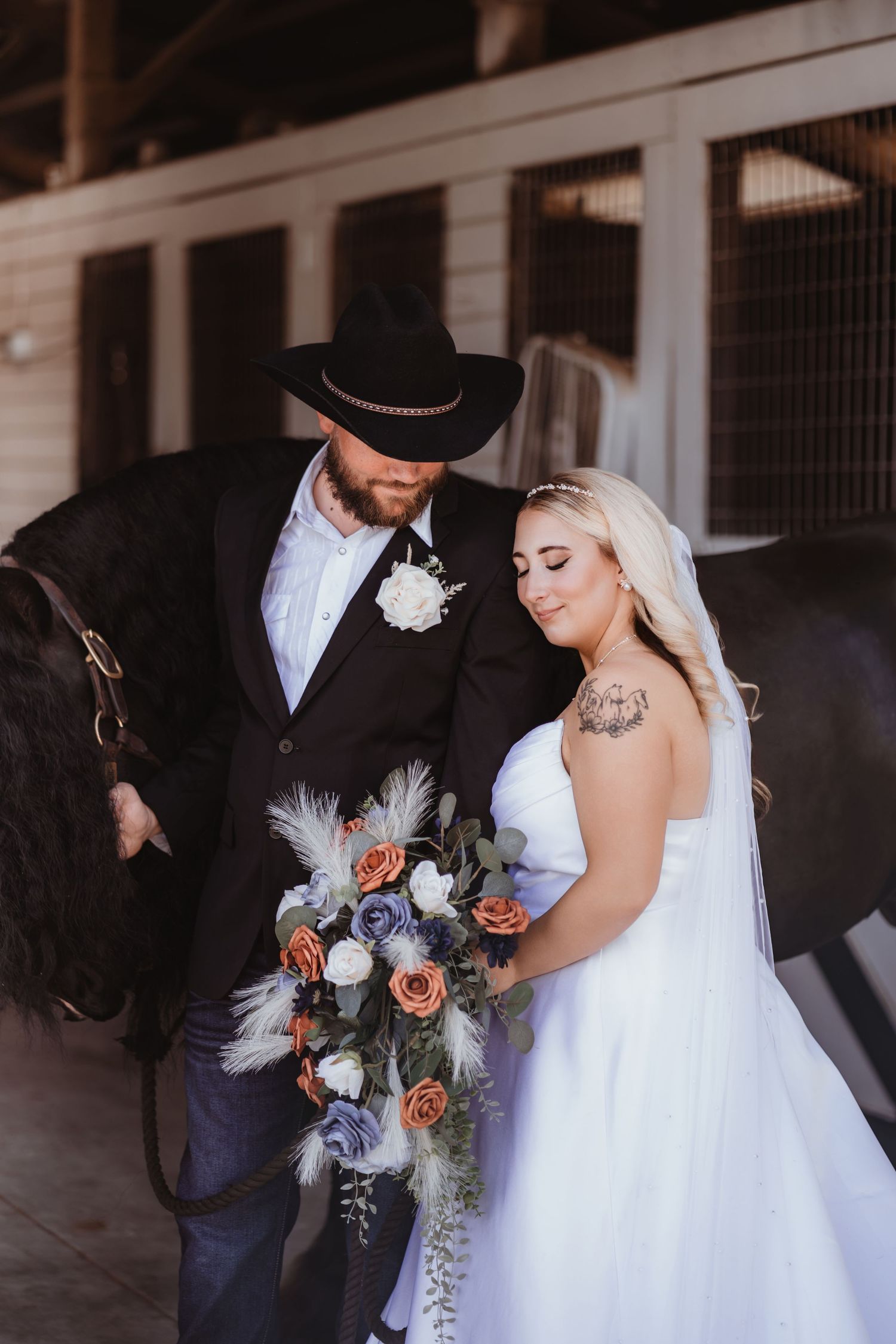 Bride and groom pose with a black horse at a rustic barn wedding venue.