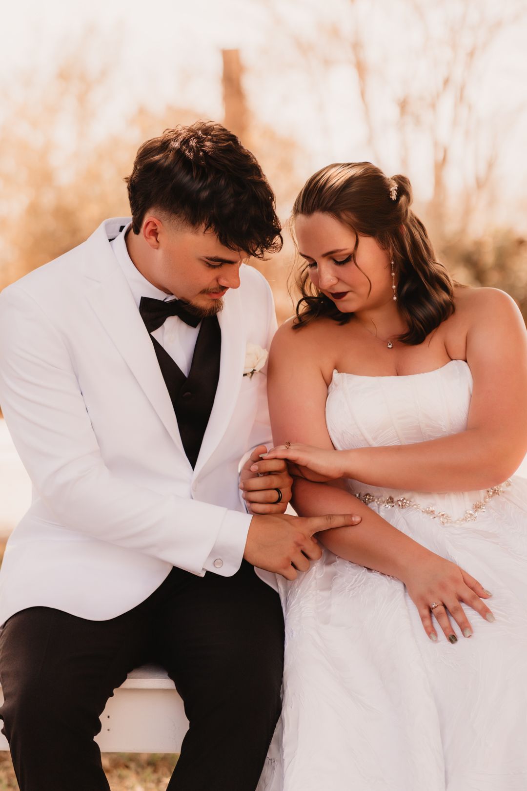 Bride and groom examining wedding rings together while seated, bathed in warm golden sunset light.
