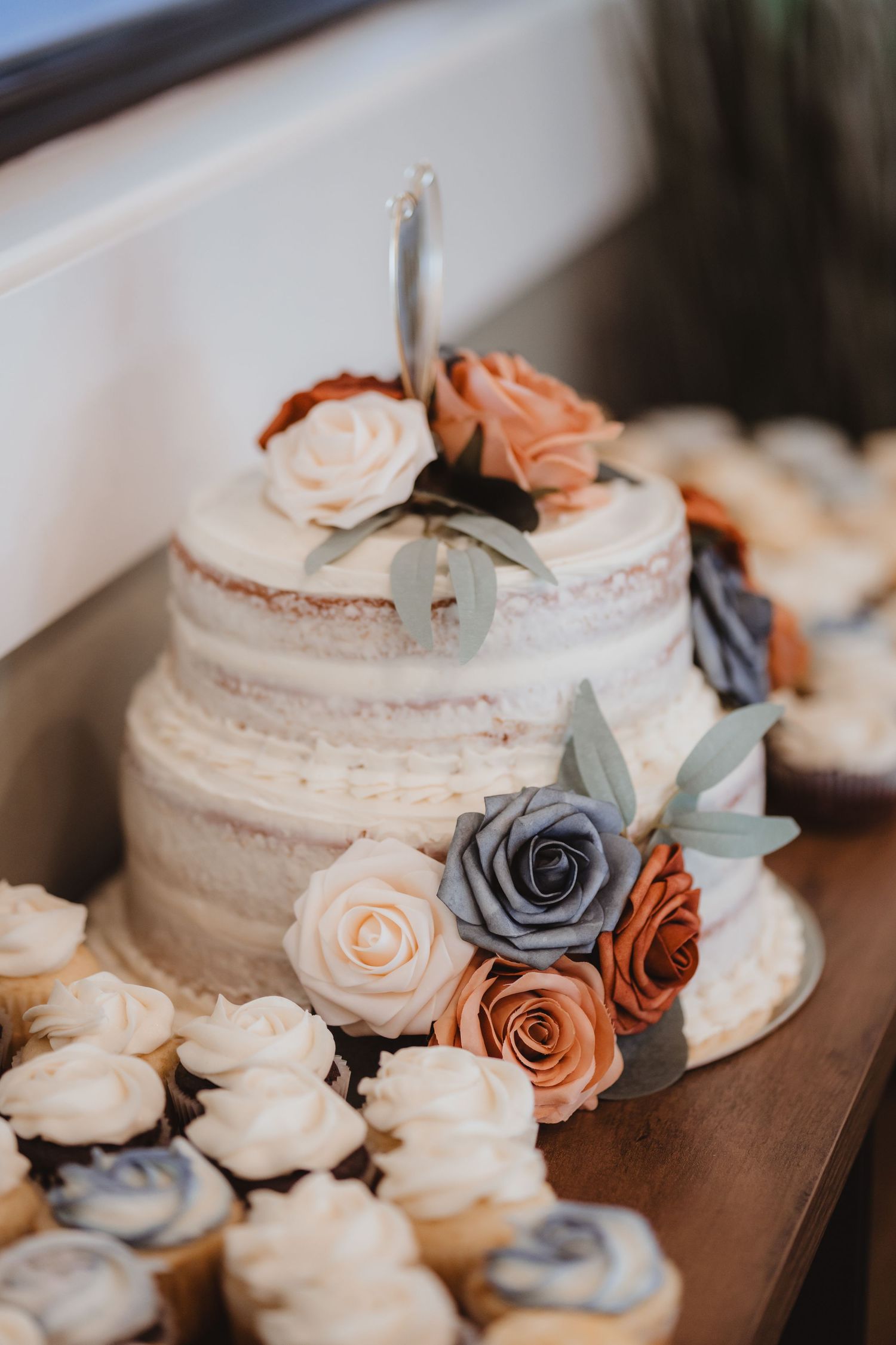 Two-tier naked wedding cake decorated with peach, blue, and rust roses and greenery.