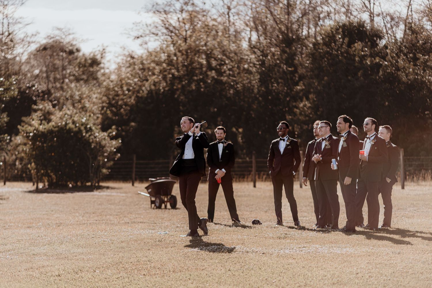 Groom leads groomsmen across an open field in dark suits during outdoor wedding photos.