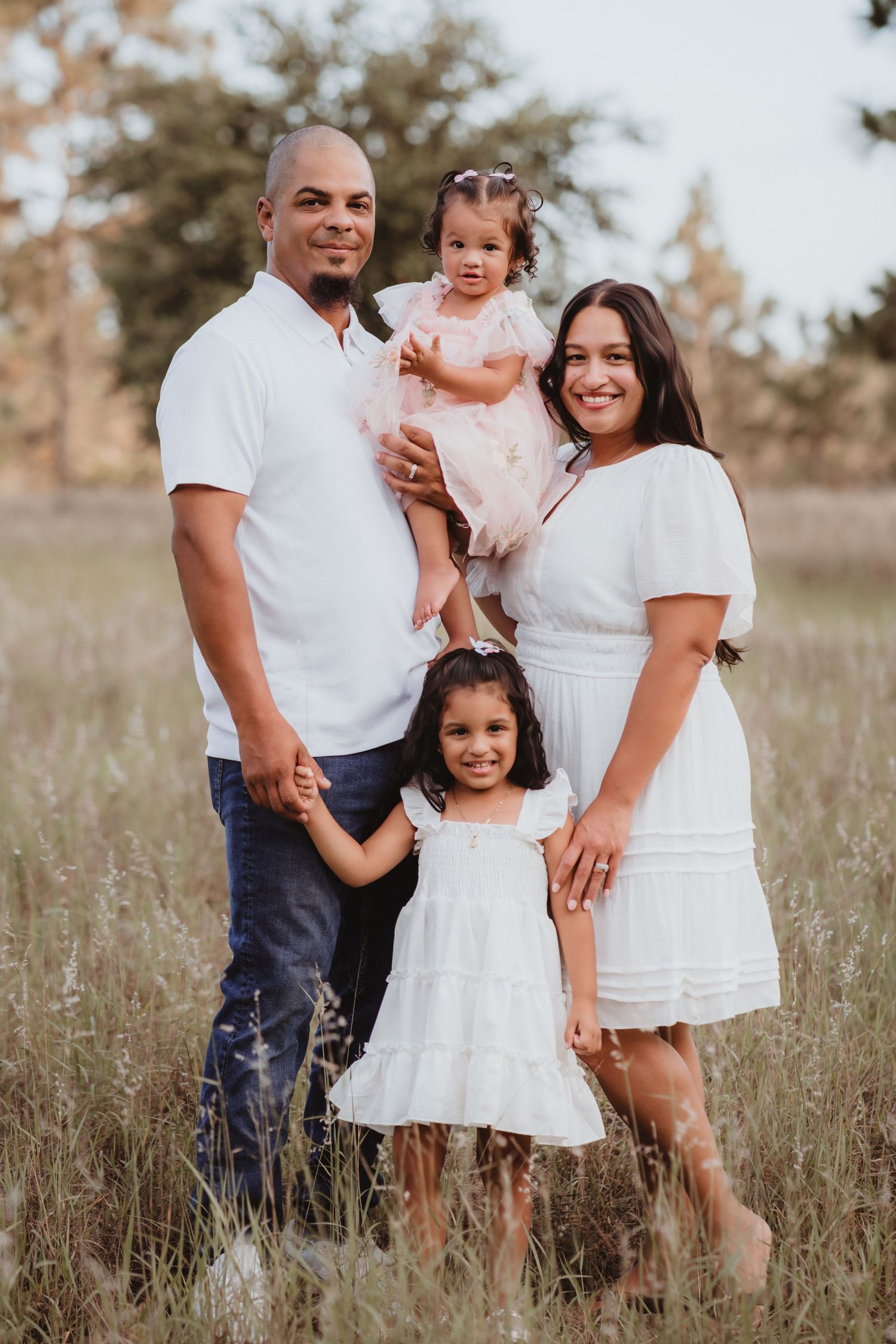 Smiling family of four posing together in a golden field, dressed in white outfits.