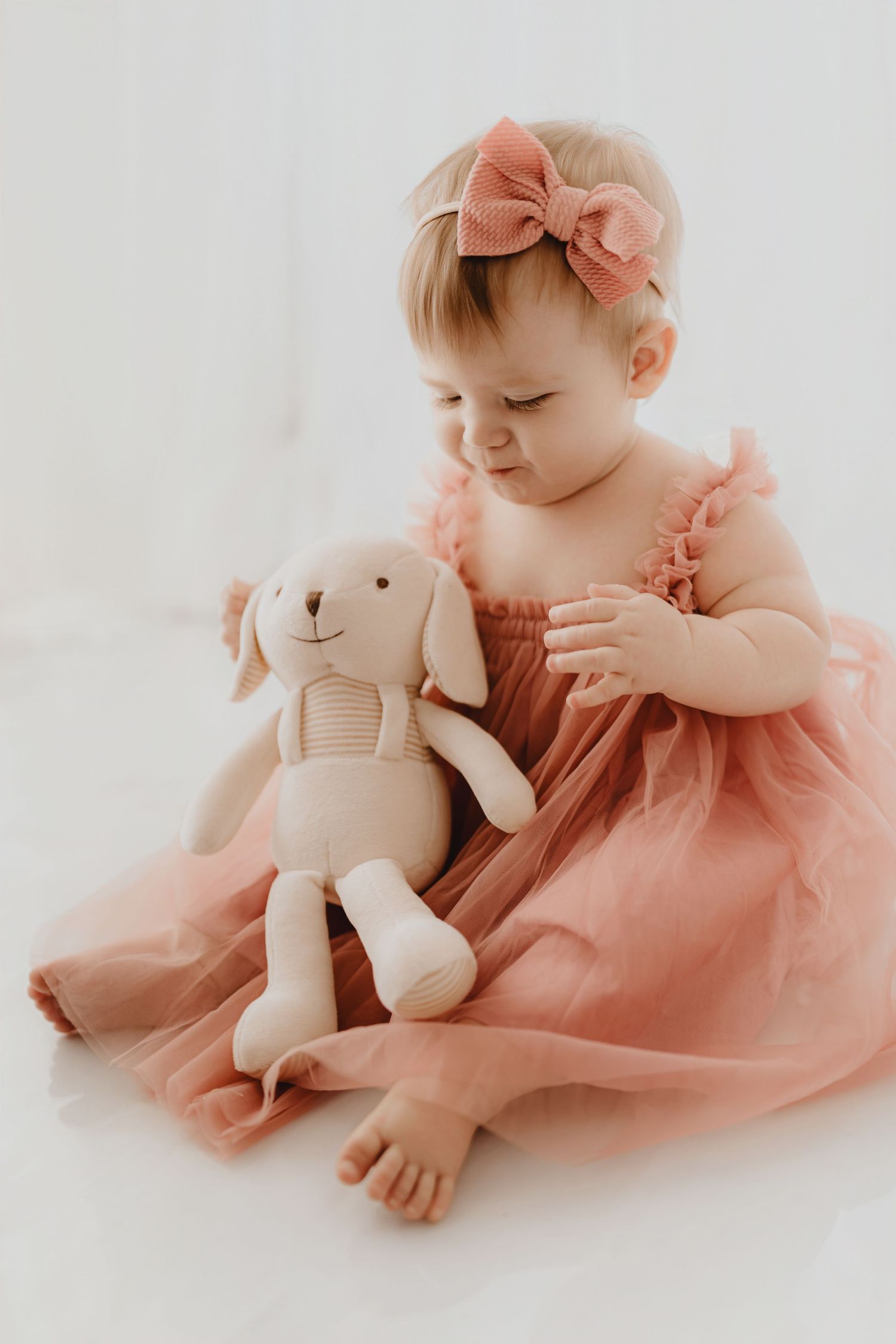 Adorable baby girl in pink tulle dress holding a stuffed bunny toy.