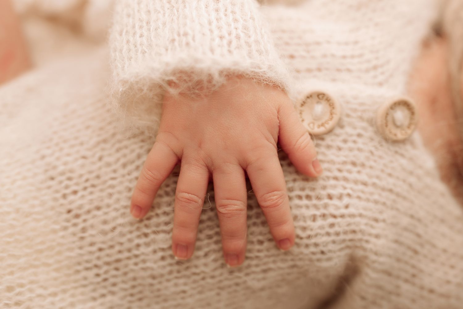 Close-up of a newborn baby's tiny hand resting on a soft cream knit blanket.