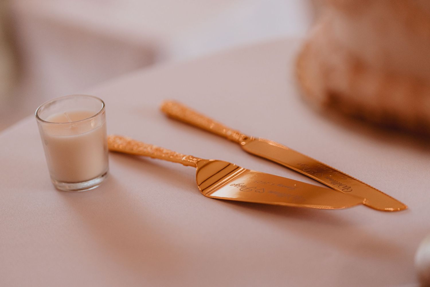 Gold rose gold cake cutting set with server and knife beside small votive candle on white table.