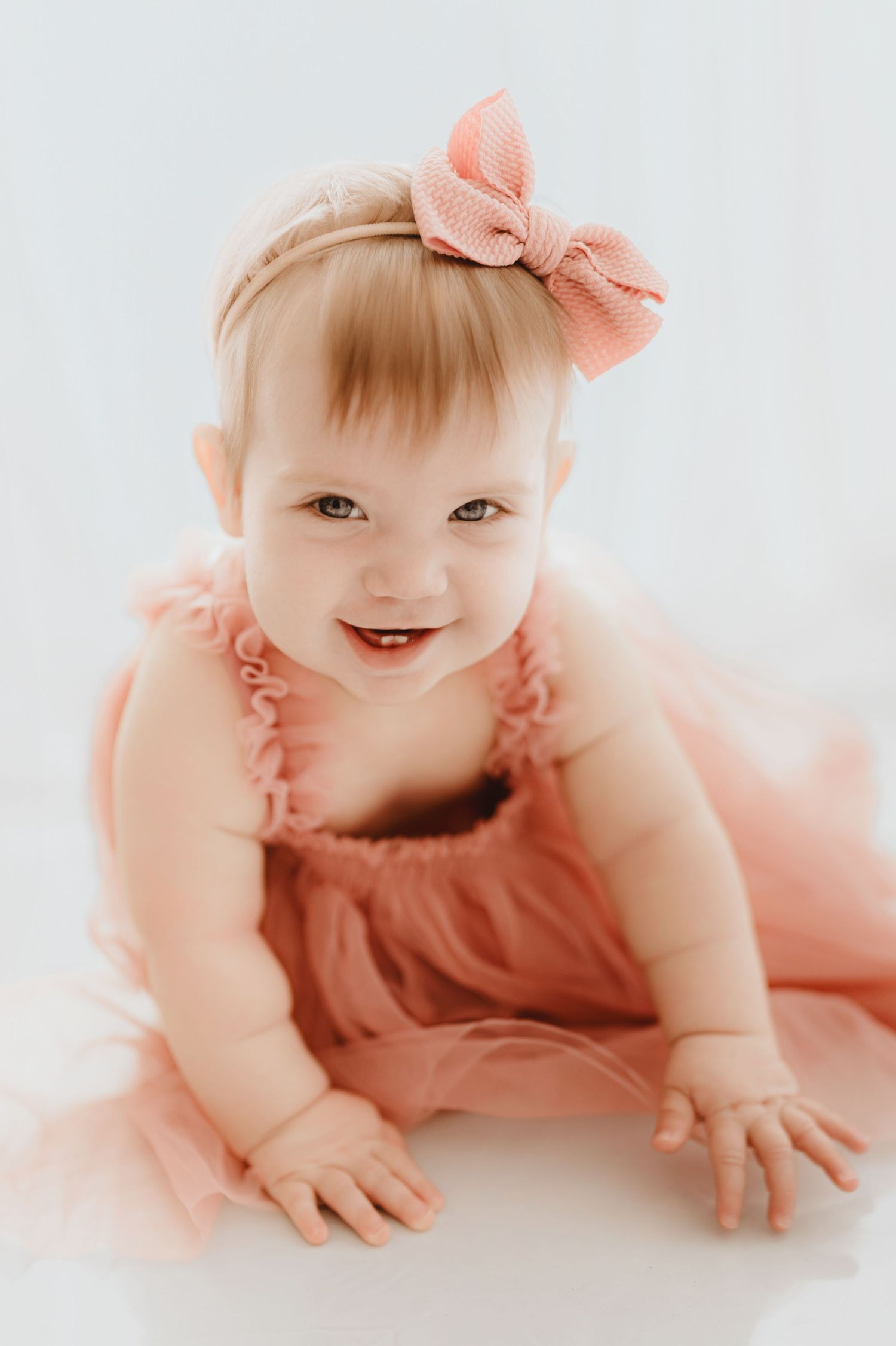 Happy smiling baby girl in pink ruffle romper and bow headband crawling forward.