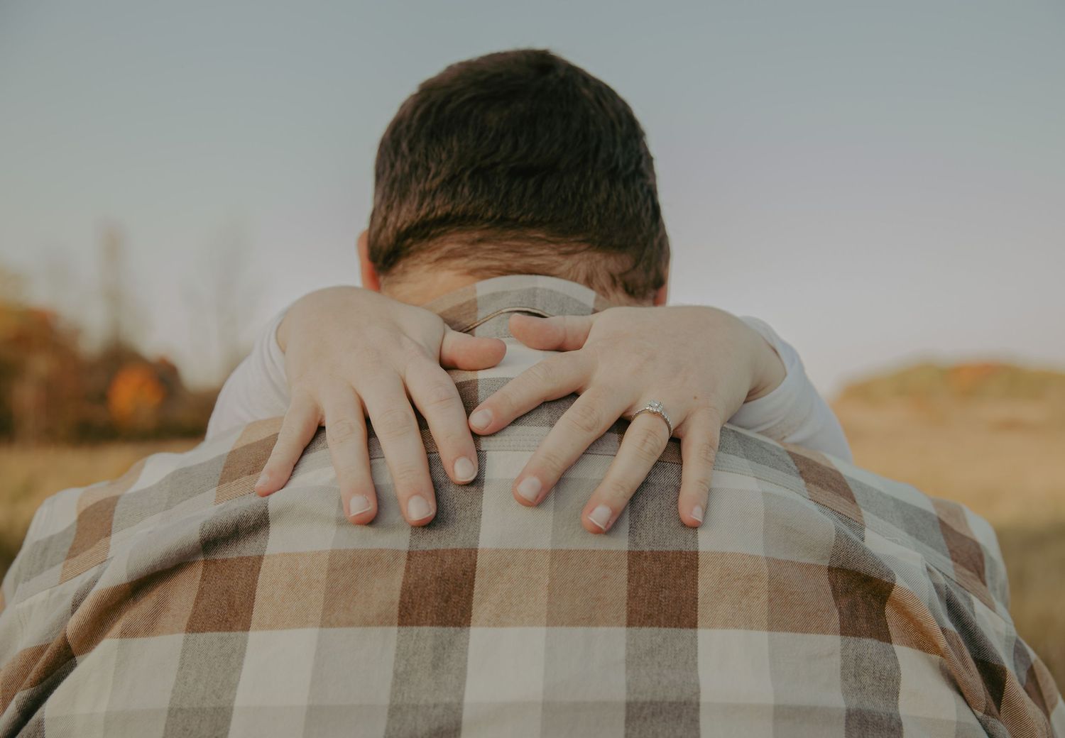 Close-up of hands wrapped around someone wearing a plaid shirt from behind.