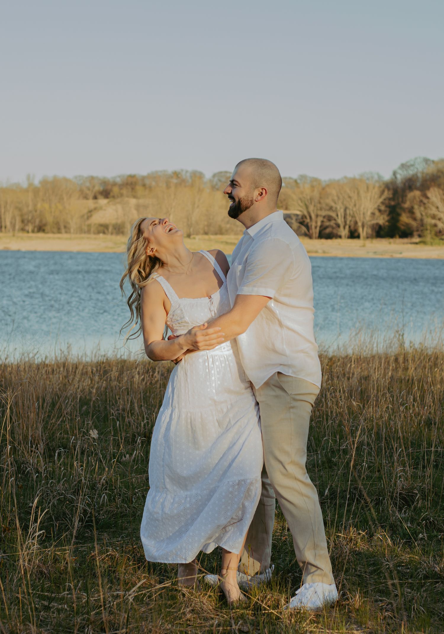 A couple shares a romantic moment by a lake during golden hour.