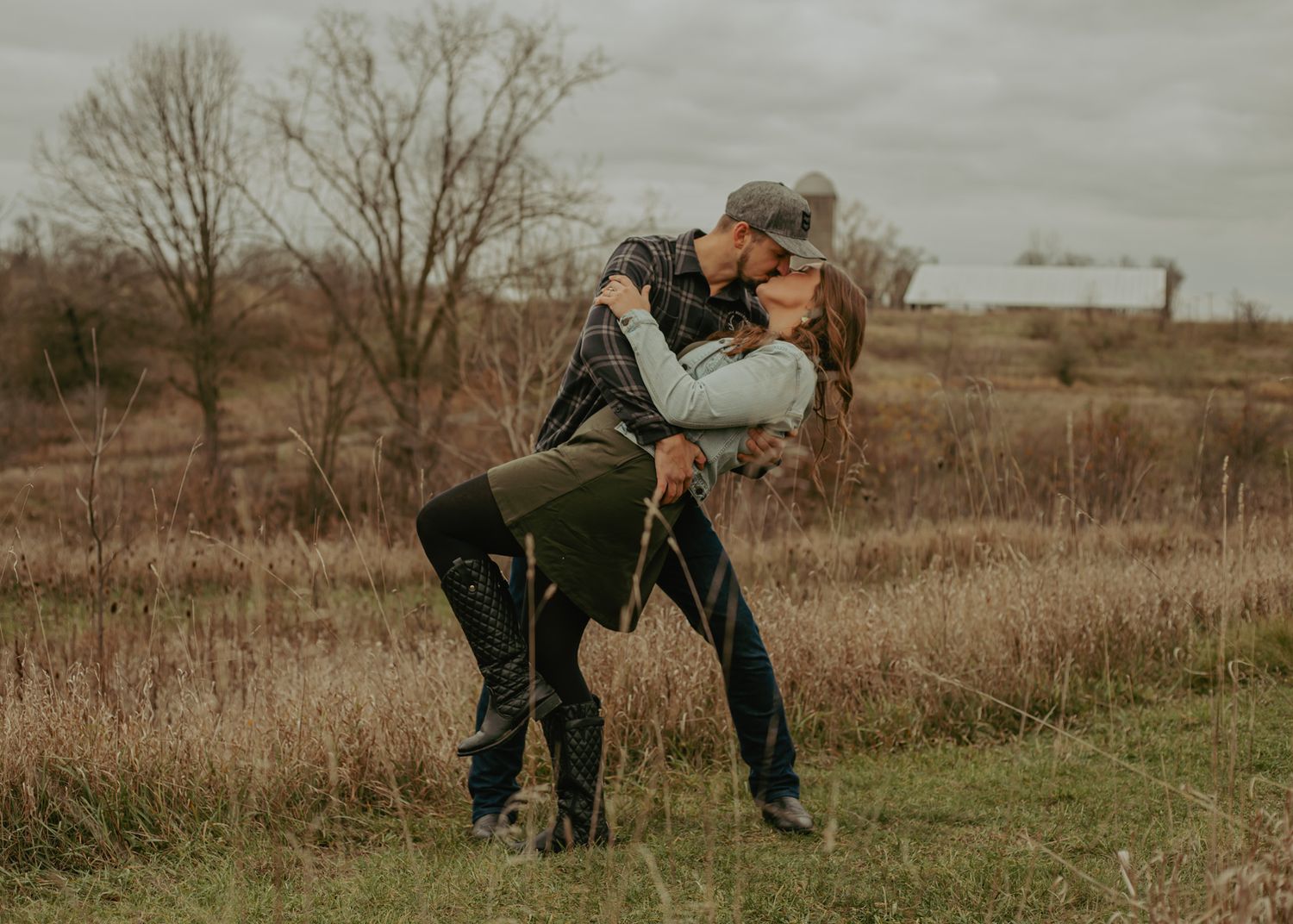 Two people playfully interact in a rustic outdoor setting with tall grass.