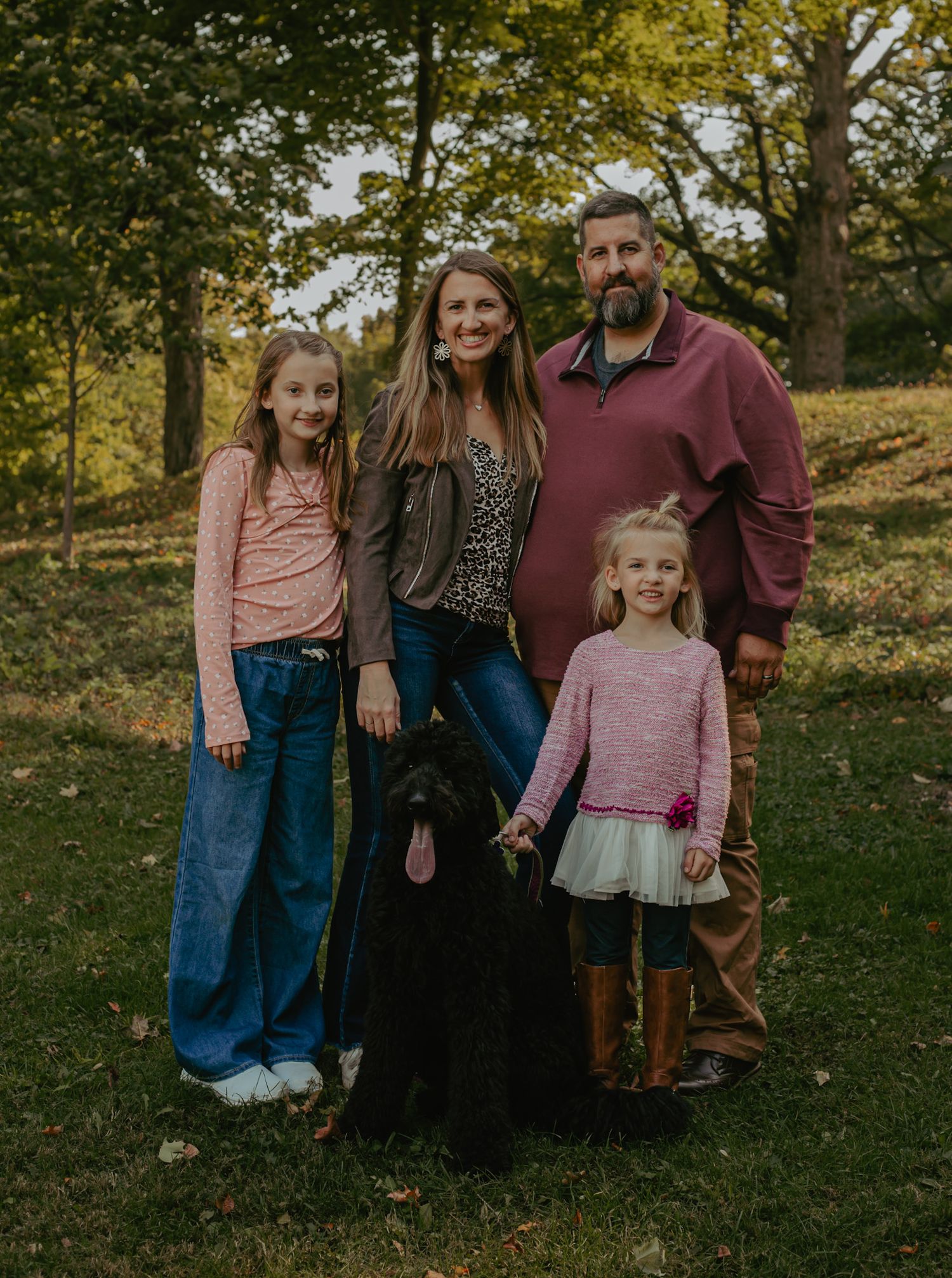 Family portrait session in a park during autumn with coordinated pink and burgundy outfits.