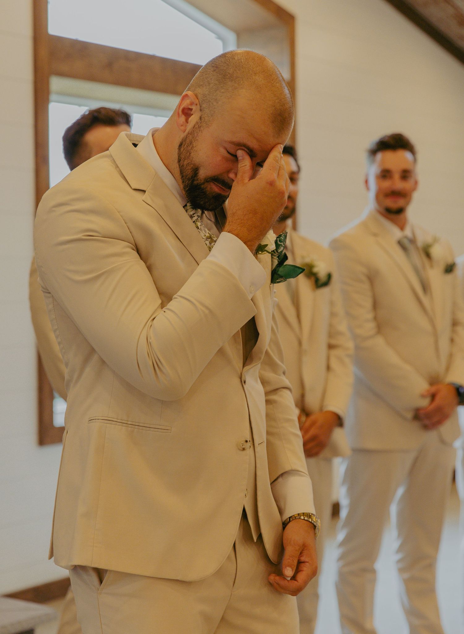 Wedding party members in cream colored suits preparing in a bright indoor space.