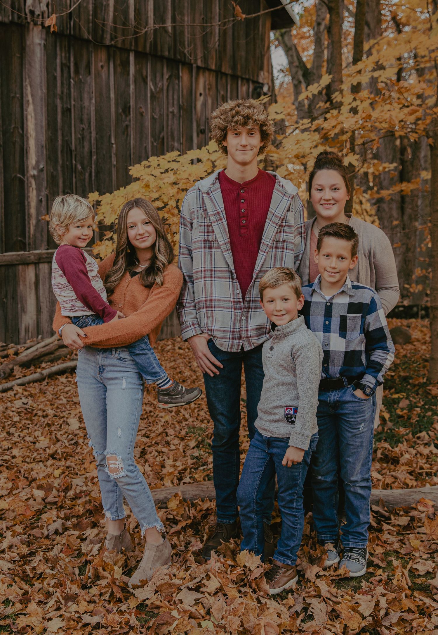 Family group portrait against wooden barn with fall foliage in background.