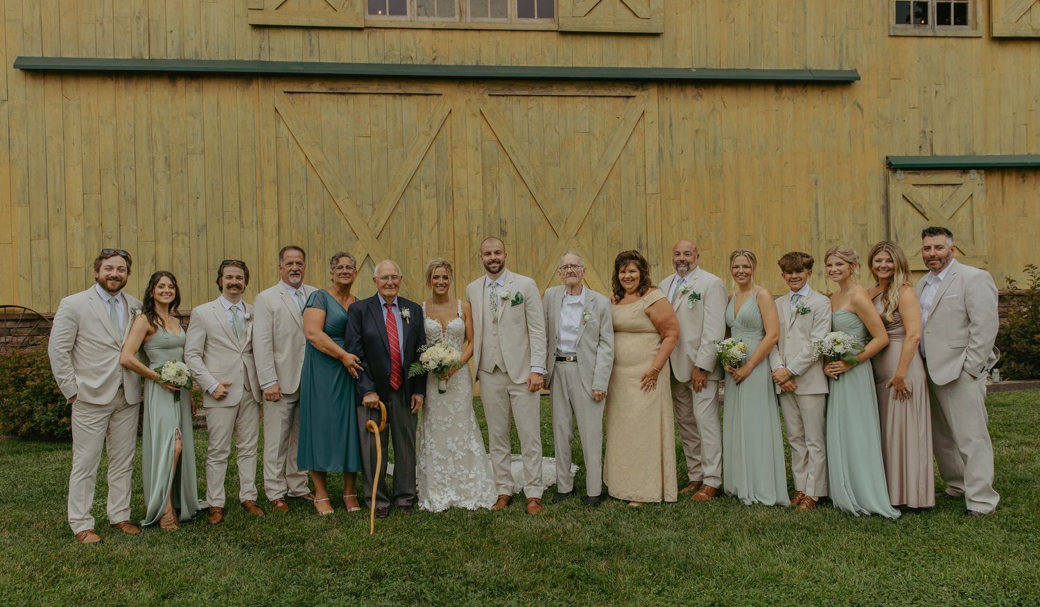 Large wedding party group photo in white and cream attire posed in front of a building.