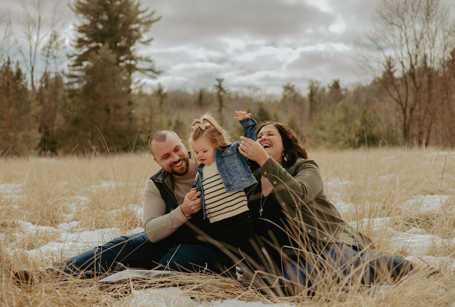 Candid family moments captured in a snowy field during winter photo session.