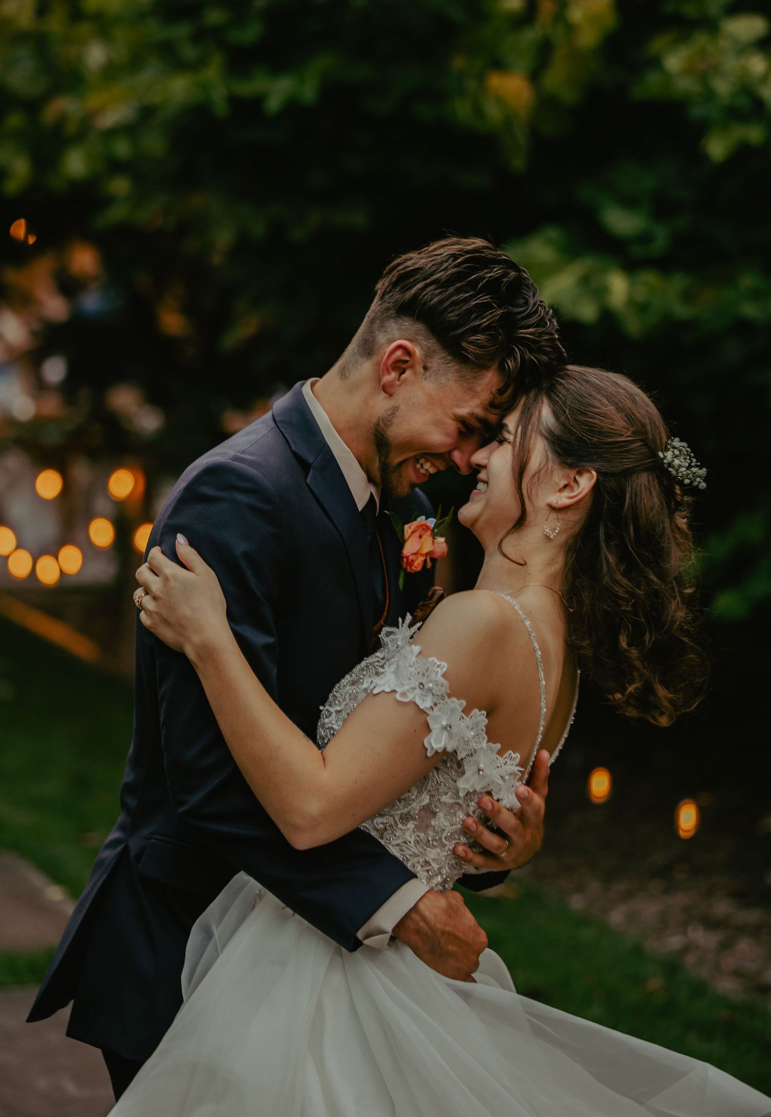 Romantic wedding couple sharing an intimate dance moment under twinkling outdoor lights at dusk.