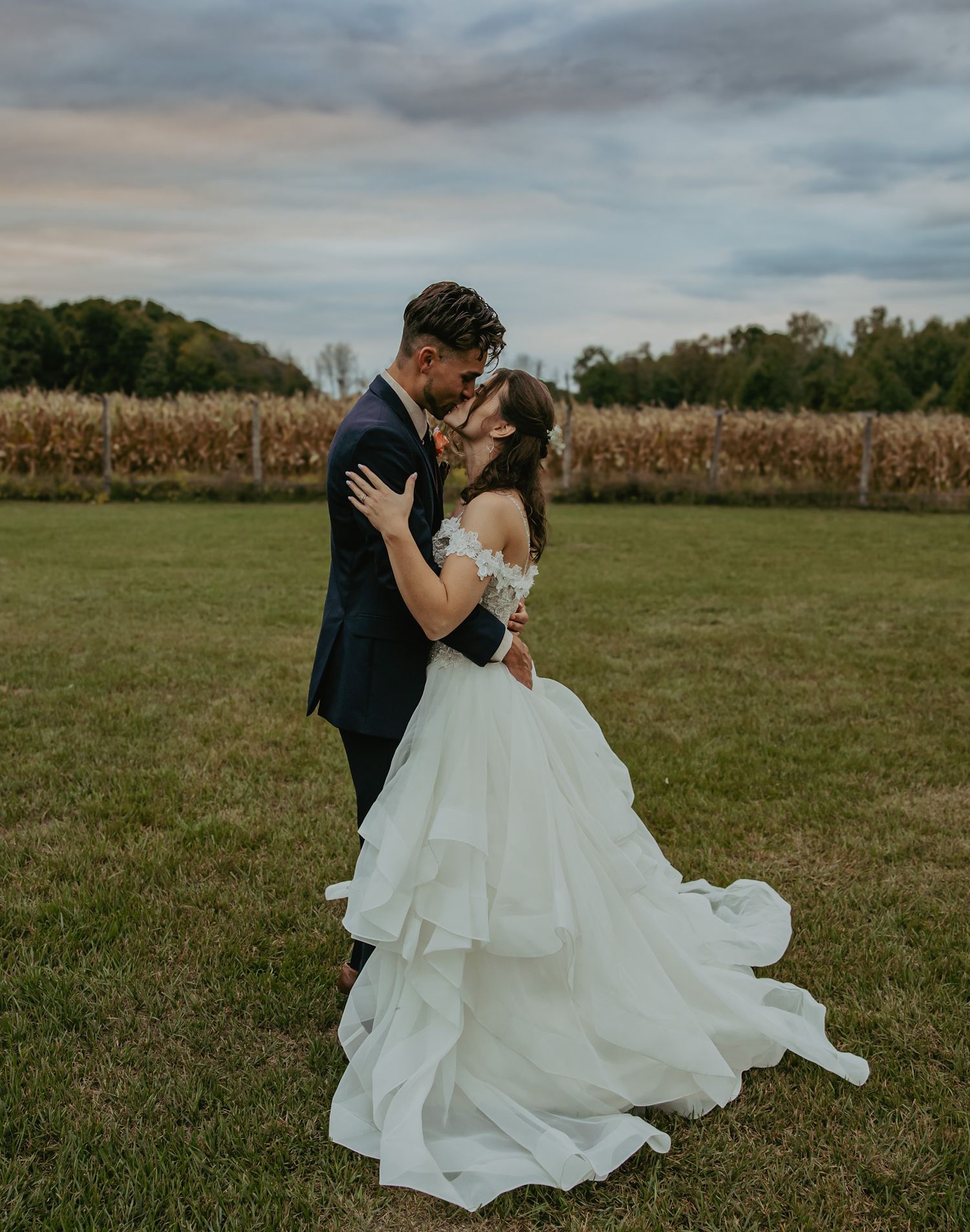A couple shares a romantic moment in their wedding attire in an open field at sunset.