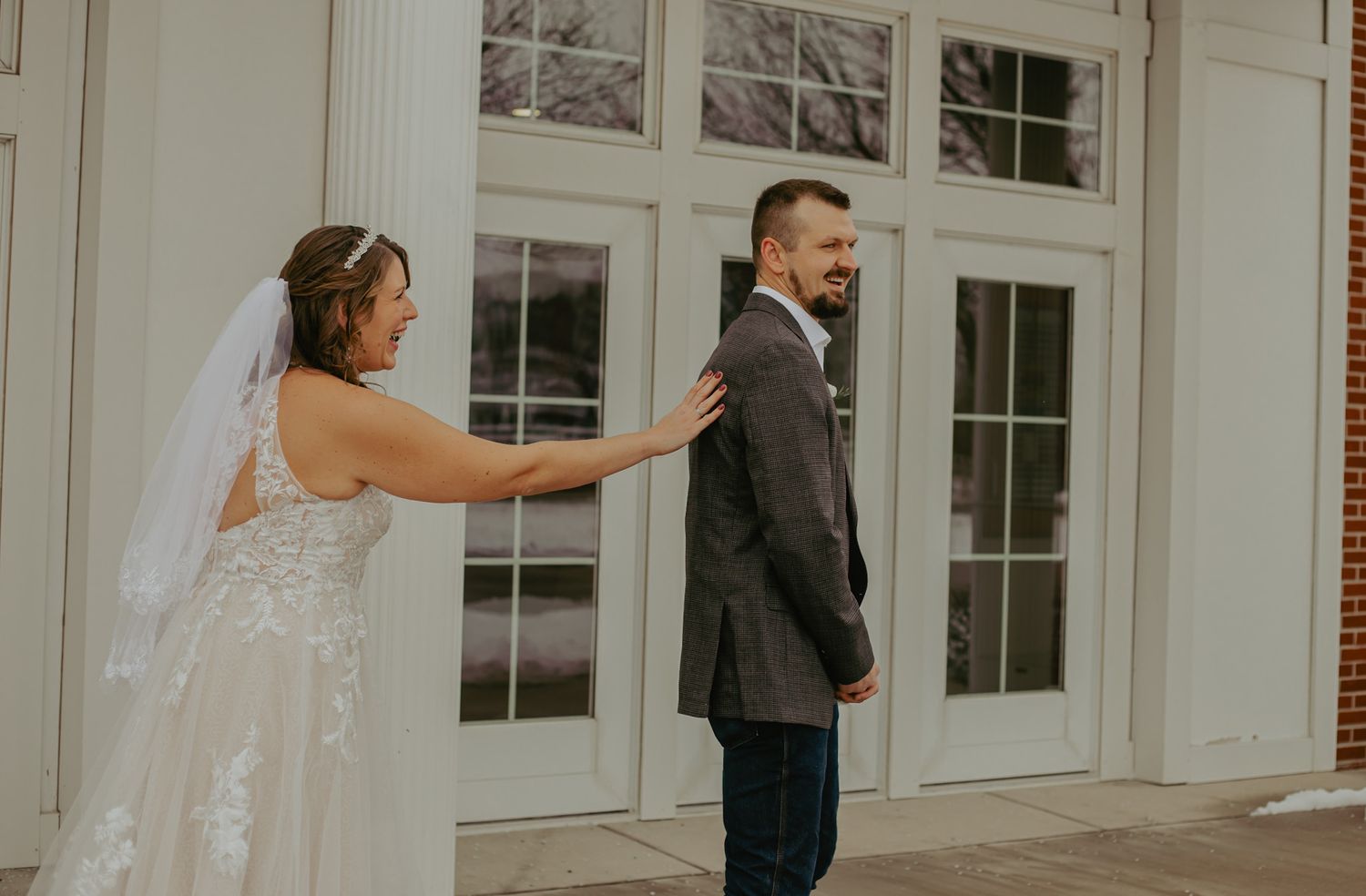 Wedding couple poses in front of elegant white columned building with windows.