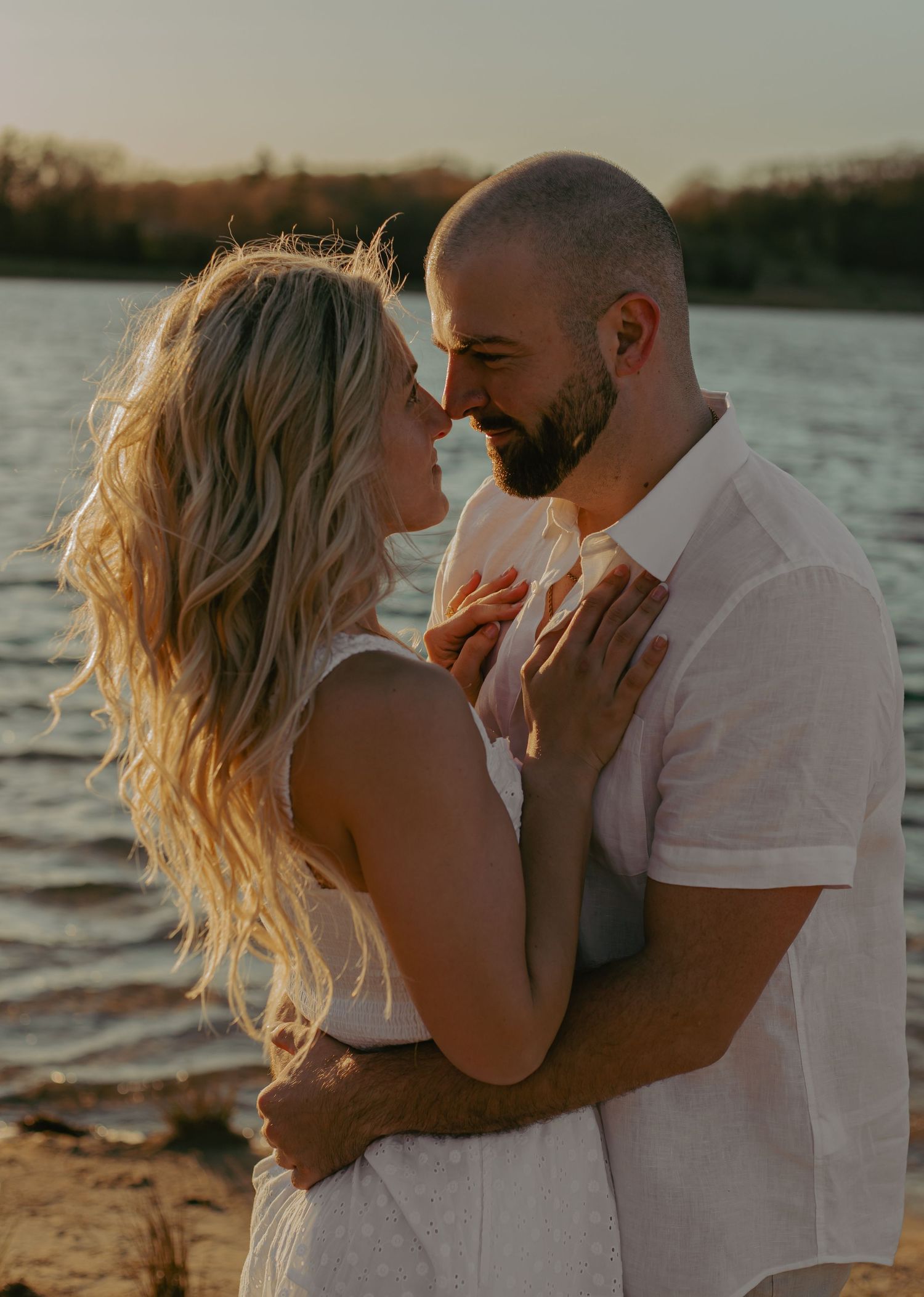 A couple shares an intimate moment at sunset by a lake.