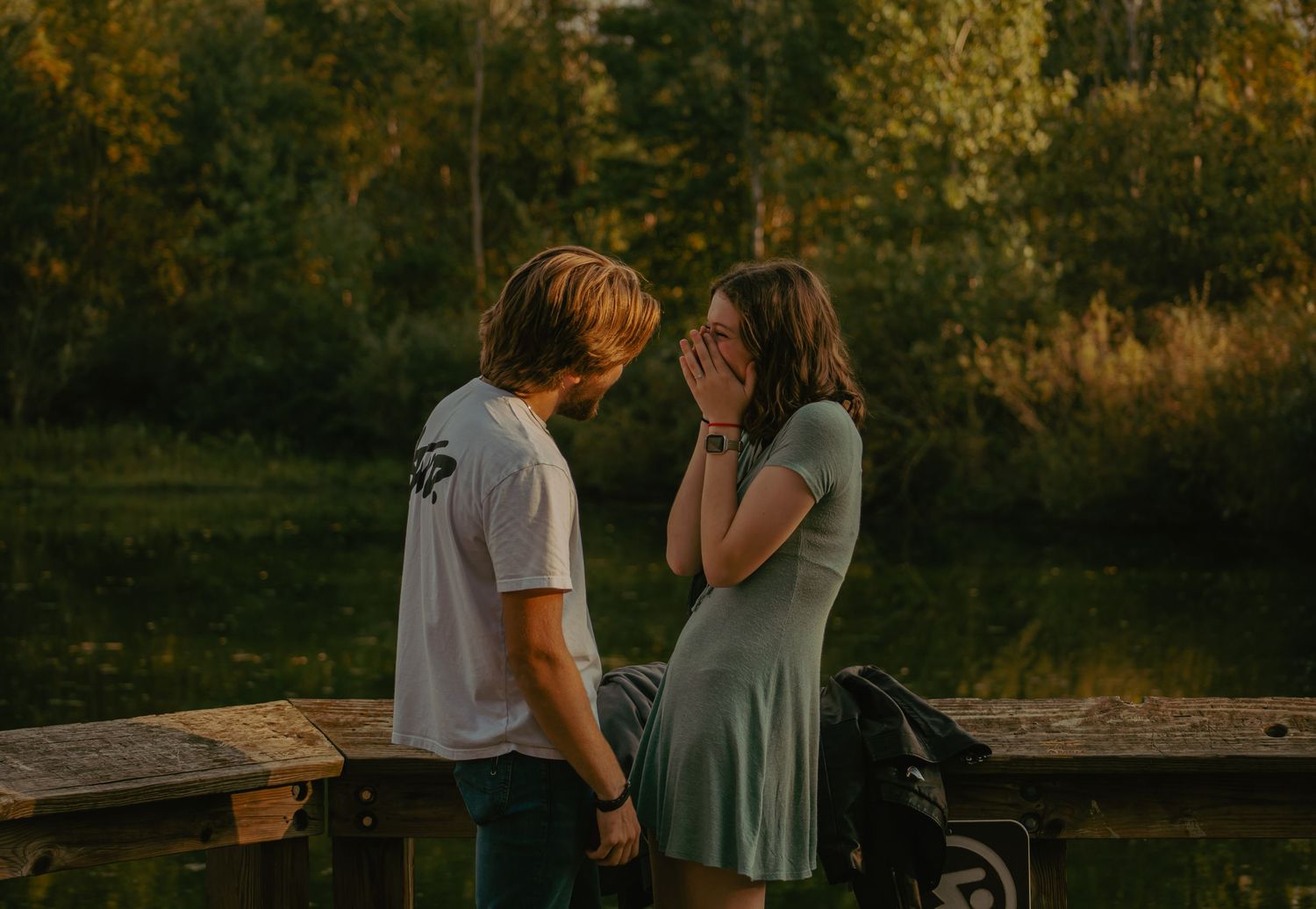 Two people share intimate moments on a dock surrounded by autumn foliage.