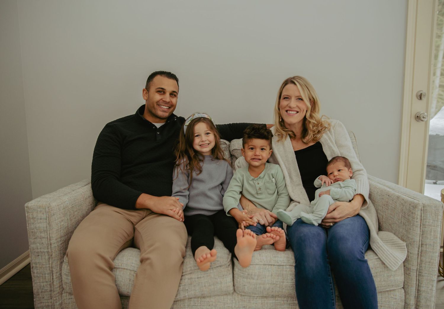 A family of five poses for a portrait while sitting on a light gray sofa.