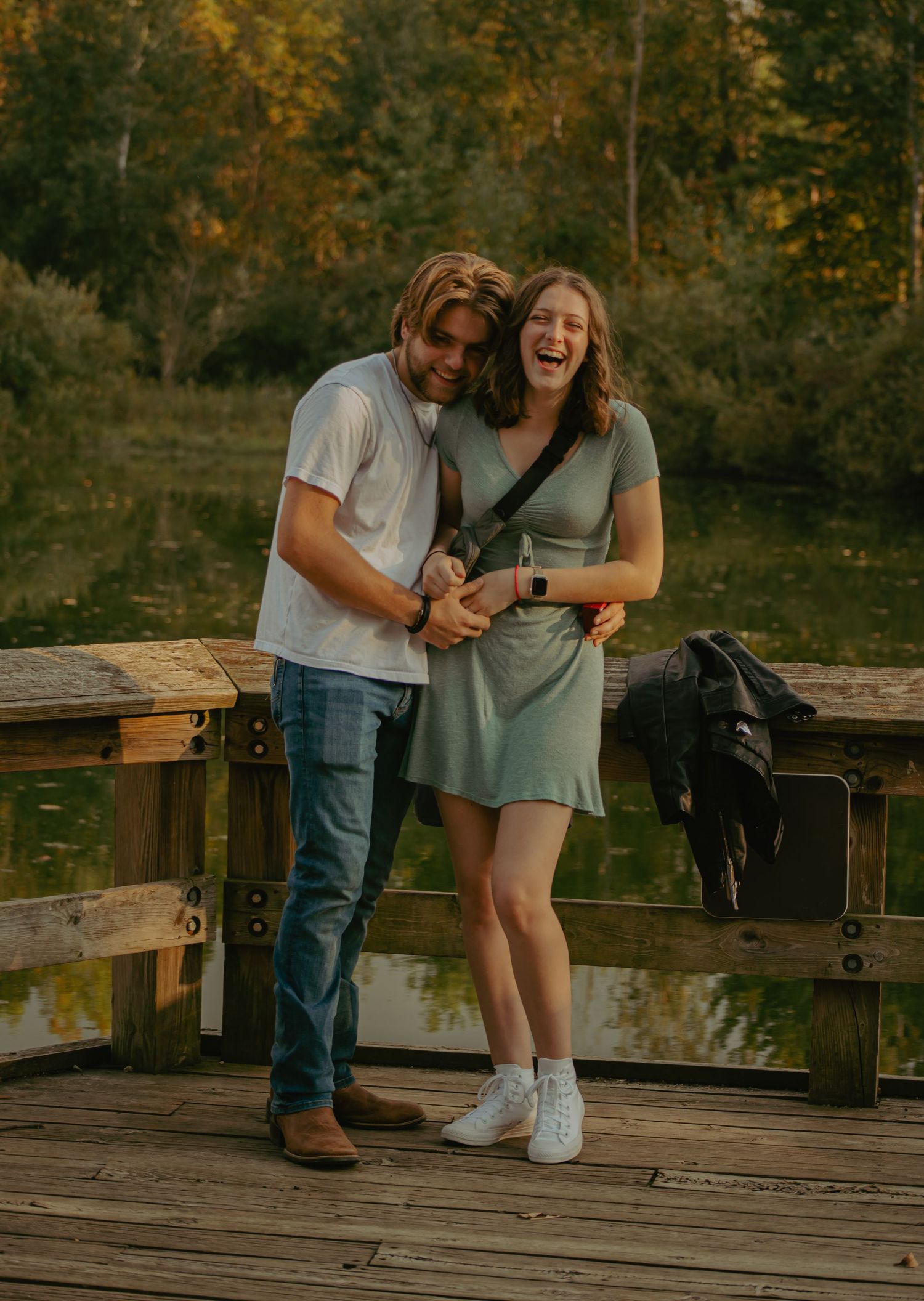 A couple shares joyful moments on a wooden dock during golden hour.