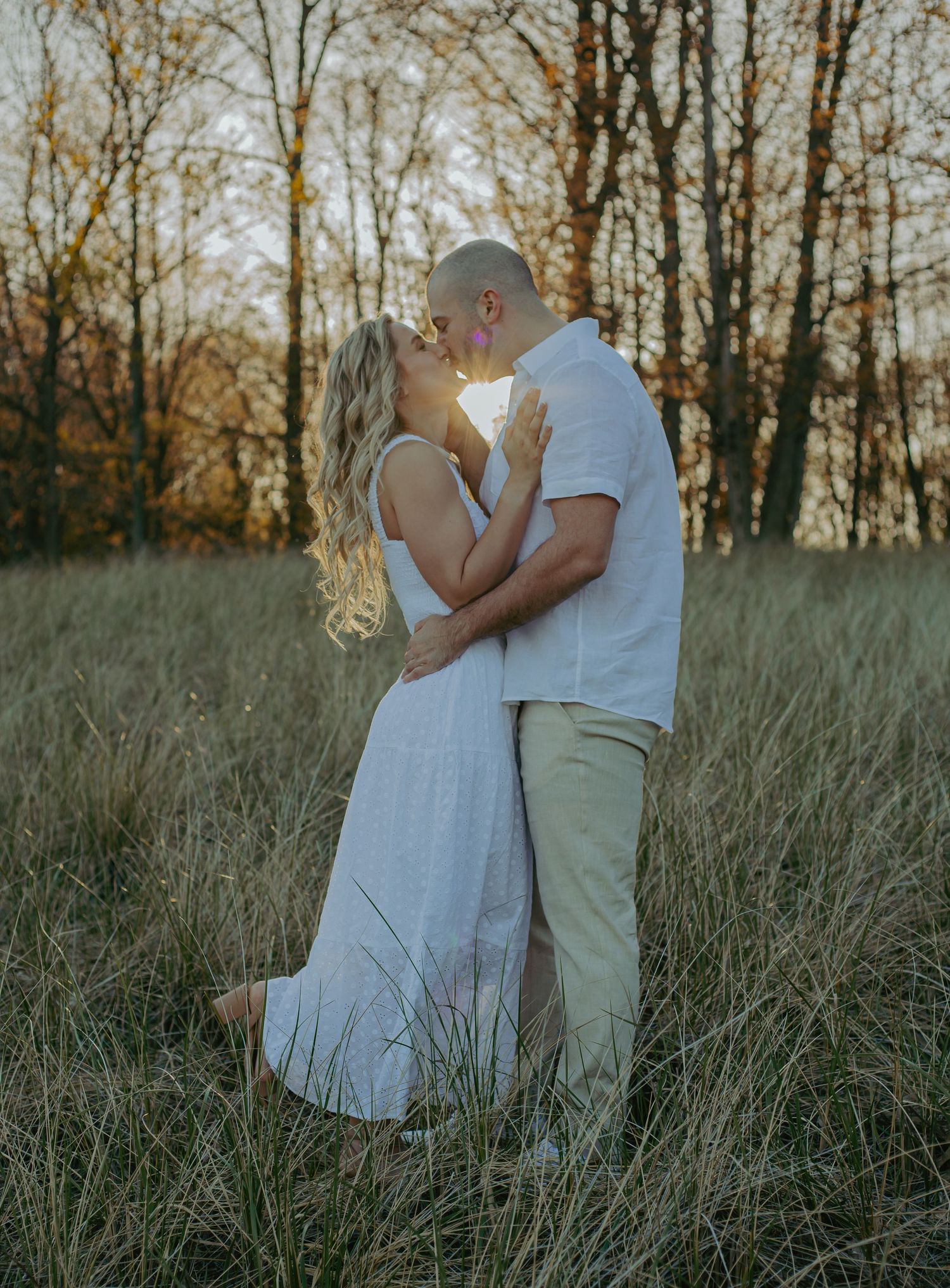 A romantic couple embraces in a sunlit field of tall grass.