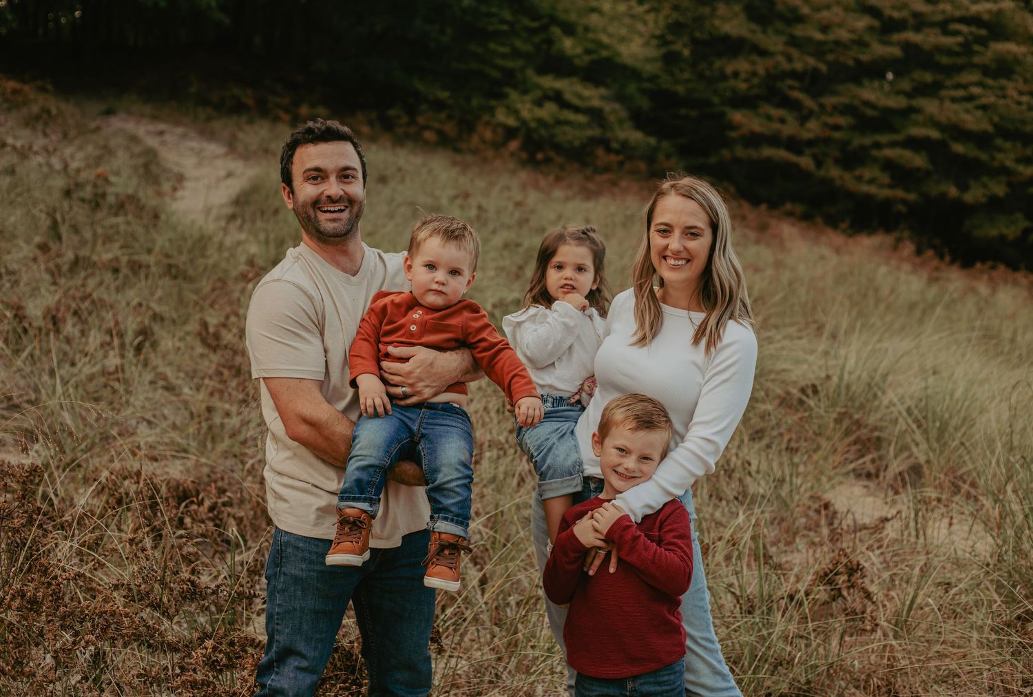 A family poses together in a grassy field during golden hour.