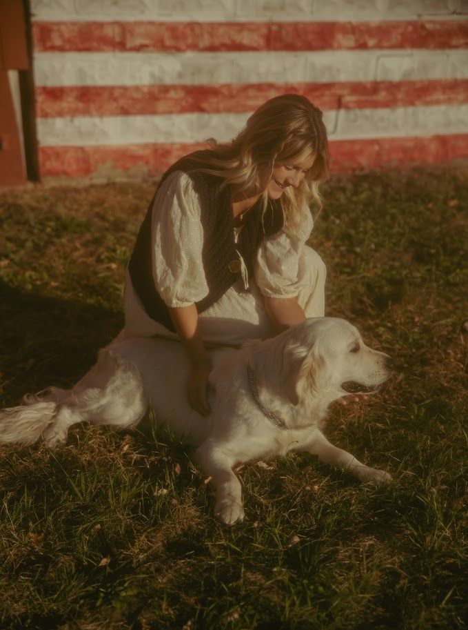 White dog plays on grass near a red and white striped wall.
