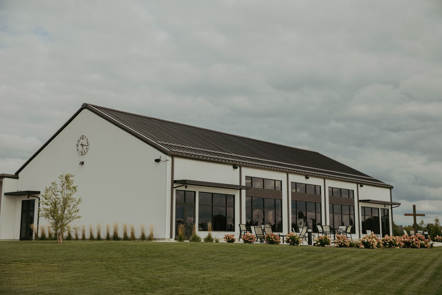 Modern white barn wedding venue with large windows and manicured lawn under cloudy skies.