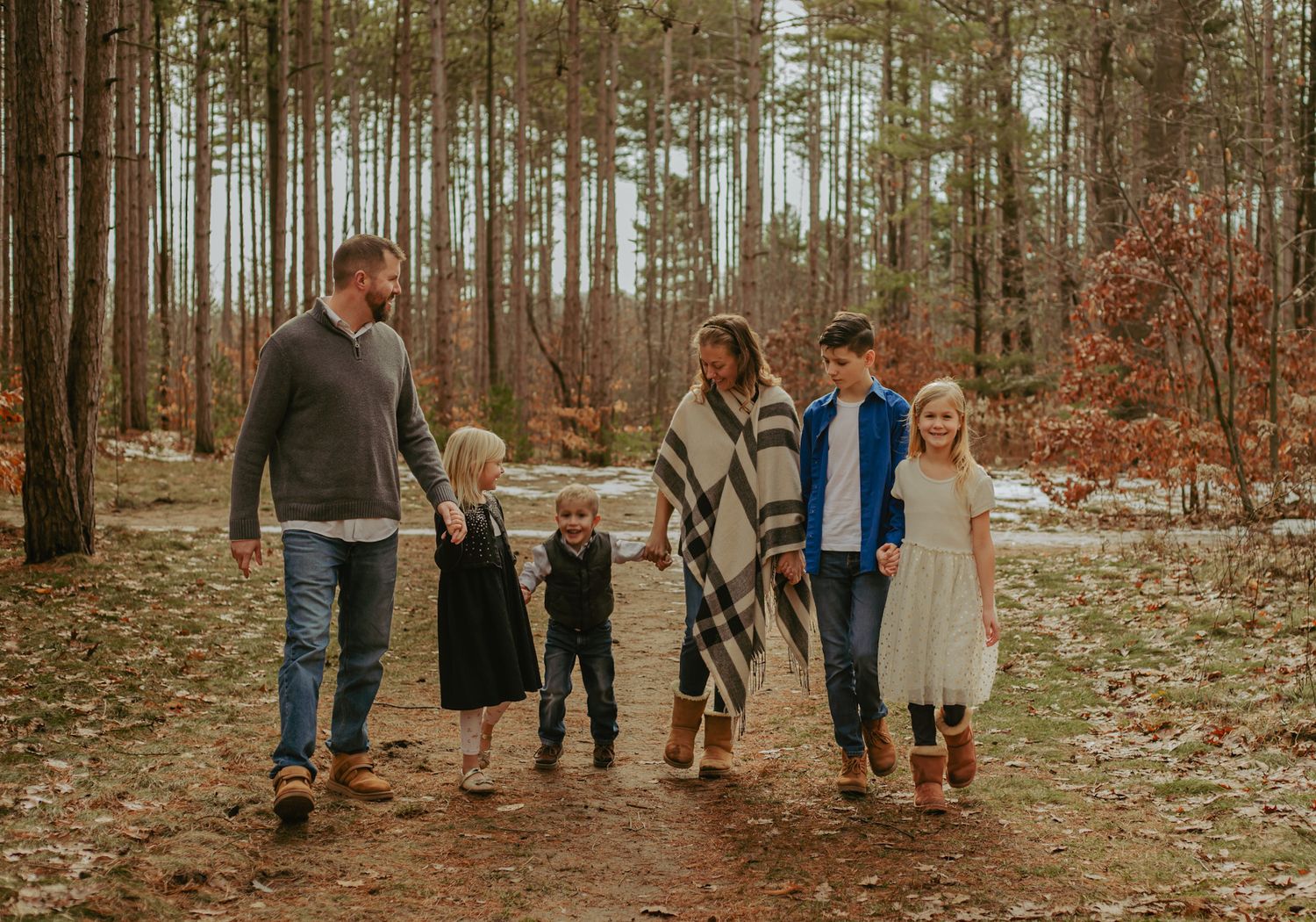 Family walking together on forest path during fall photo session.