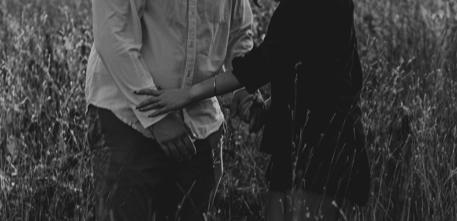 A person stands in tall grass in black and white, with only their torso and hands visible in the frame.