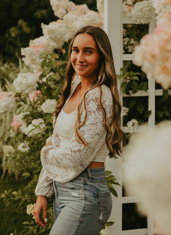 Fashion portrait with white lace crop top and jeans against blooming roses and white fence.