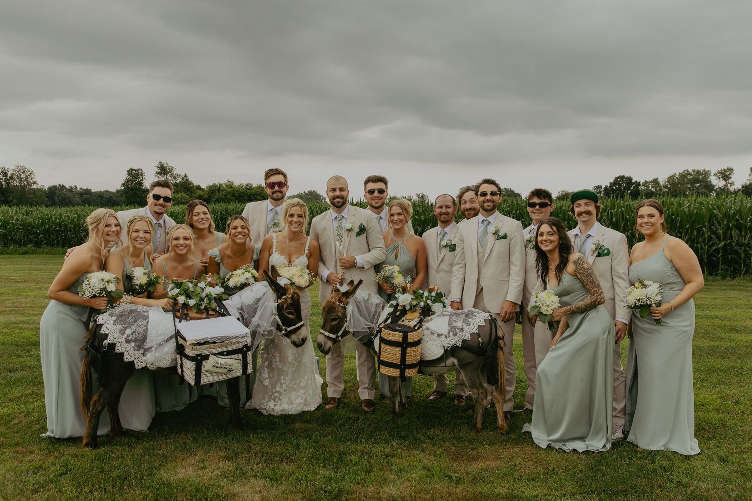A large wedding party in grey attire poses together in an outdoor field setting.