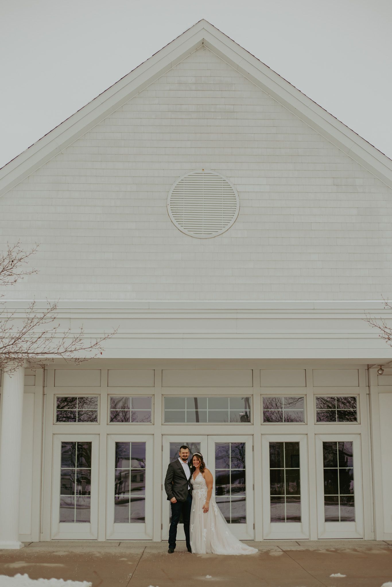 White chapel exterior with large windows and a circular detail in winter setting for a wedding ceremony.