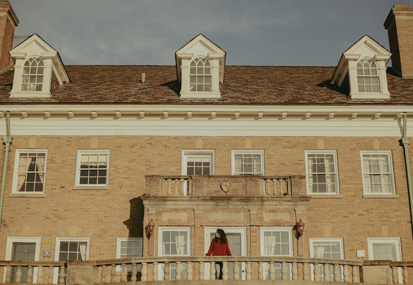 Exterior view of large brick building with white dormers and colonial architecture.