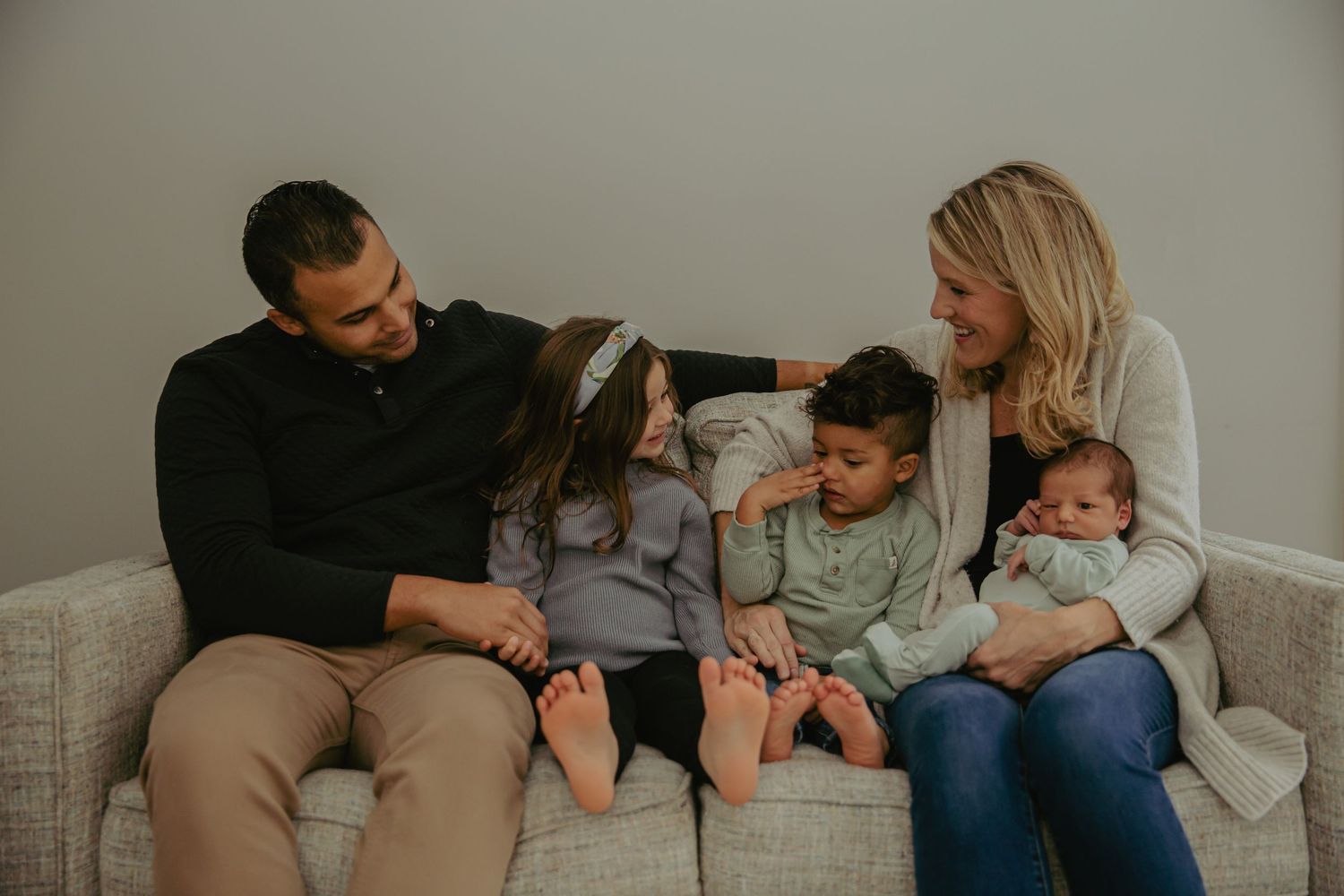 A family relaxes together on a gray couch in an intimate indoor setting.