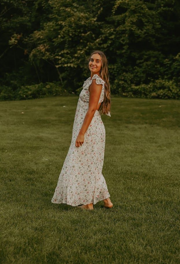 Figure in flowing white dress twirling on lush green lawn during golden hour.