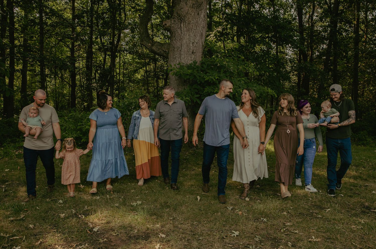 Large family group walking together in a lush green forest setting, wearing coordinated earth-tone outfits.