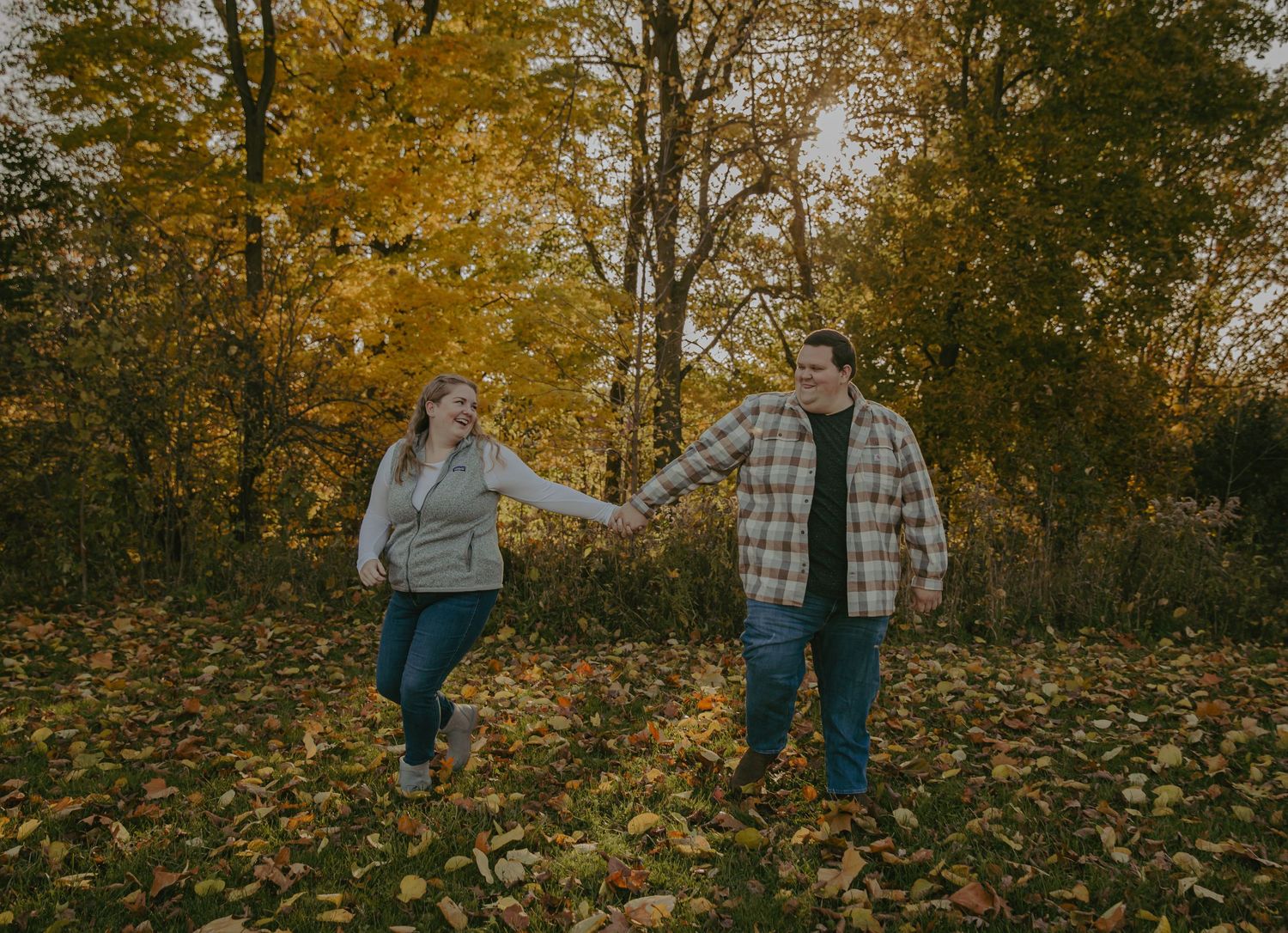 Playful couple holding hands while jumping in autumn leaves.
