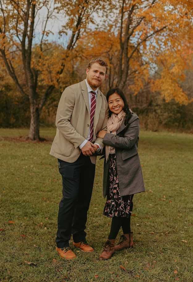 Couple shares joyful moment together on autumn grass with orange trees in background.
