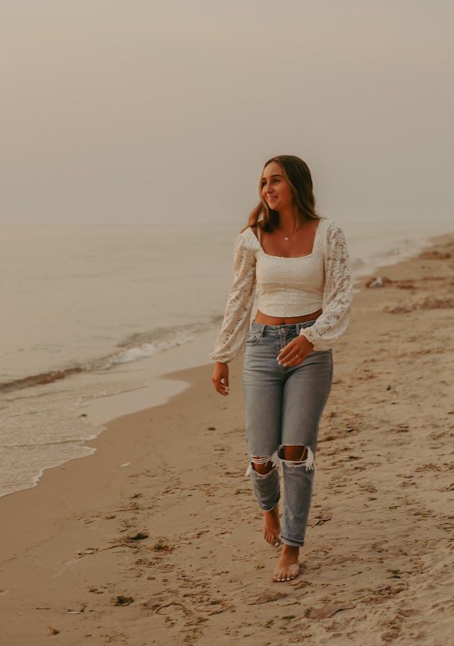 Casual beach photoshoot featuring white lace top and distressed jeans along the shoreline.