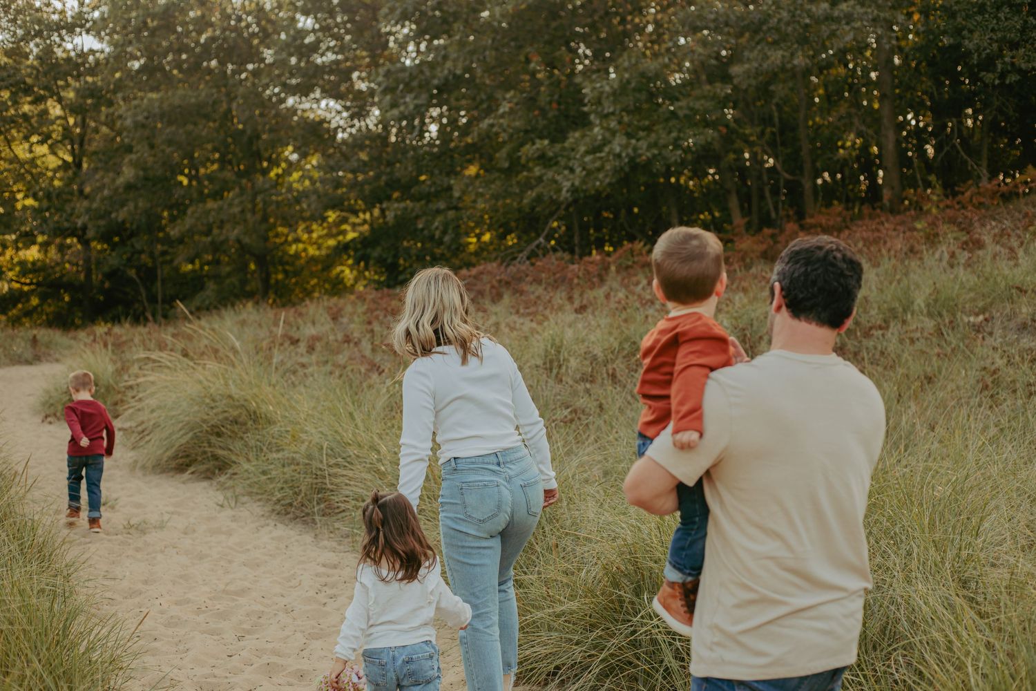 A family walks together on a winding path through tall grass at sunset.